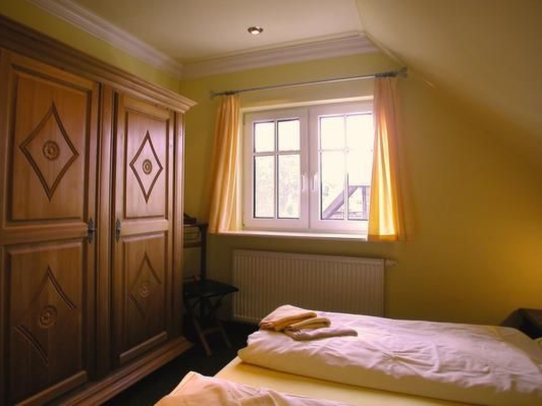 Et værelse med to senge, et træskab, et vindue med gardiner og en radiator.