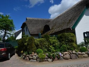 Ein traditionelles Haus mit einem Strohdach, einer Steinsäule und üppiger Bepflanzung davor.