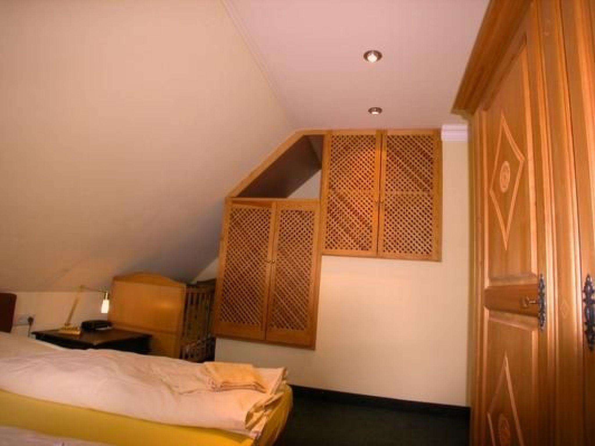A bedroom with a bed, a wooden wardrobe, and a small desk with a chair.