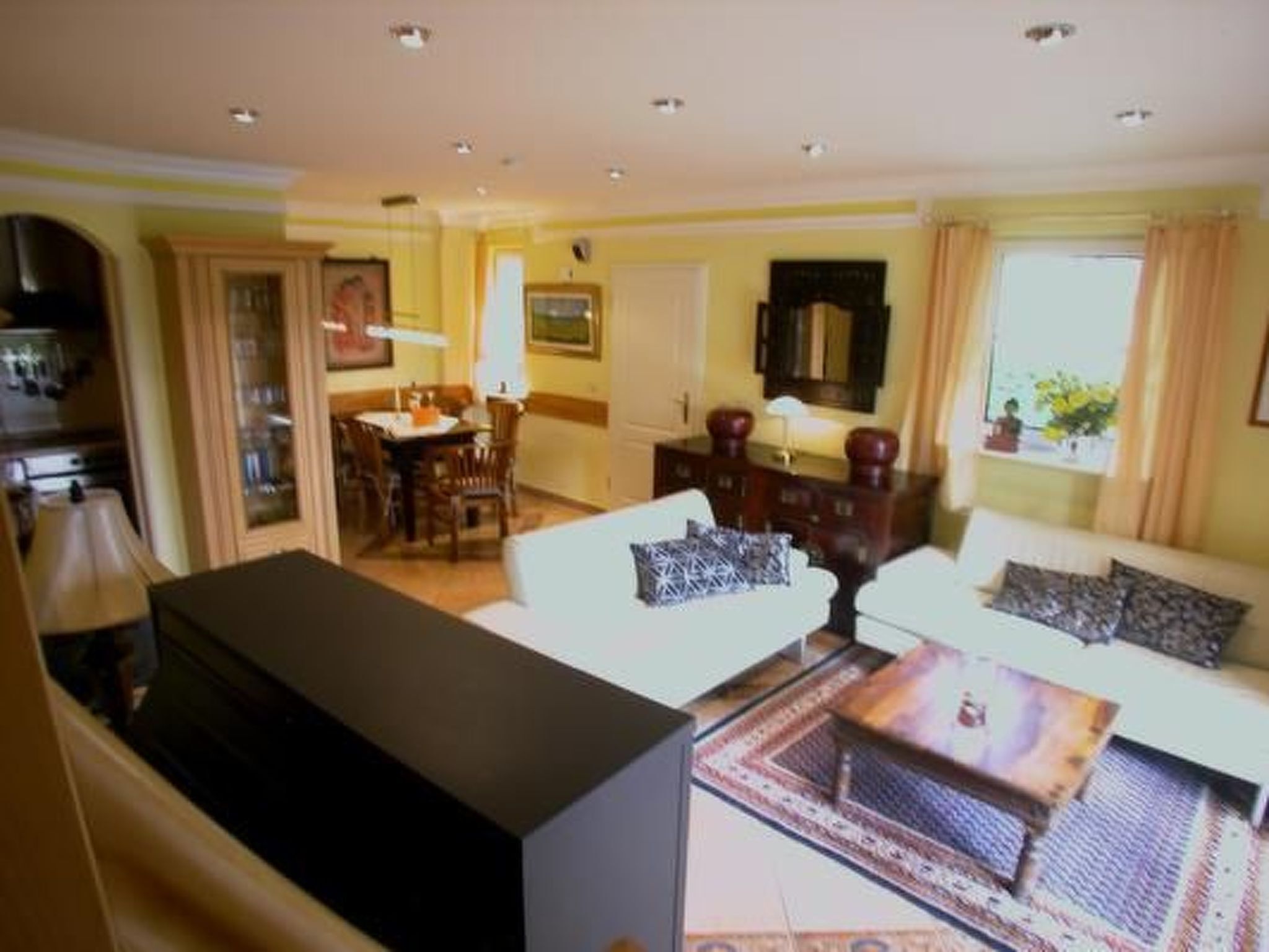 Ein Wohnzimmer mit einer Couch, einem Couchtisch und einem Fernseher. Es gibt einen Essbereich mit Tisch und Stühlen.