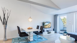 Ein modernes Wohnzimmer mit Essbereich, Fernseher und großem Fenster.