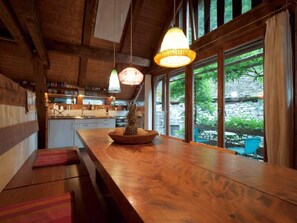 Een houten interieur met een keukenhoek, grote ramen en een houten tafel met een fruitschaal.
