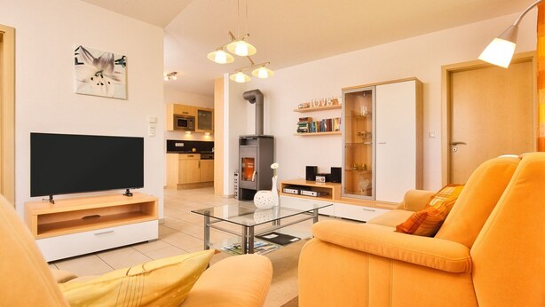 Een moderne woonkamer met een bank, een televisie, een glazen salontafel, en een keuken op de achtergrond.