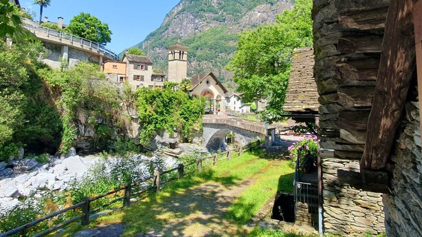 A stone bridge over a river, surrounded by lush greenery and traditional buildings.