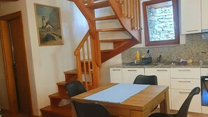 A dining area with a wooden table and chairs, a kitchen with white cabinets, and a wooden staircase.