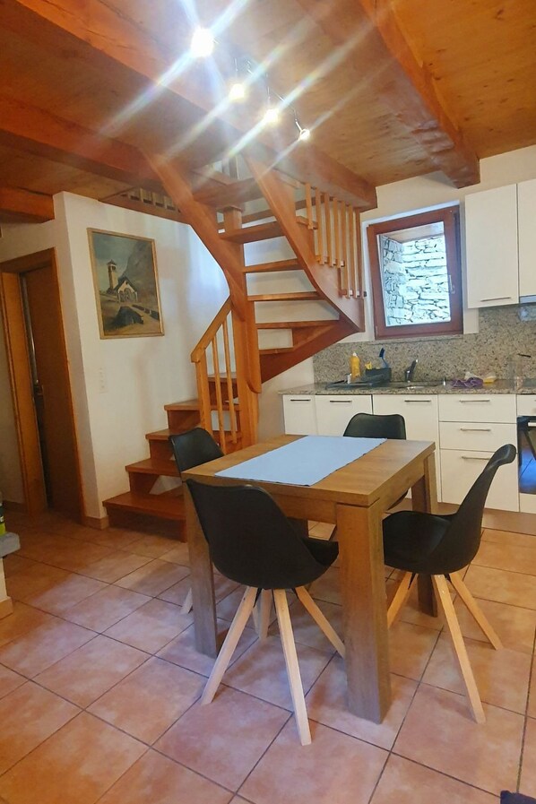 Un comedor con una mesa y sillas de madera, una cocina con armarios blancos y una escalera de madera.