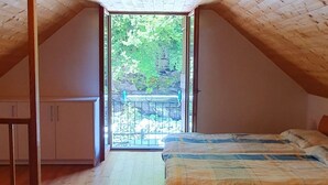 A bedroom with a wooden ceiling, a bed, a wardrobe, and a view of a balcony with greenery.