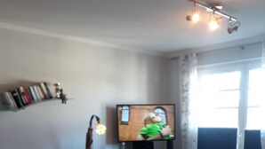 Un soggiorno con una poltrona a dondolo nera, un divano verde, un tavolino in legno e un televisore su un supporto in legno.