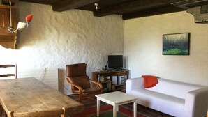 Un salon avec une table en bois, un fauteuil en cuir marron, un canapé blanc et un téléviseur posé sur un meuble en bois.