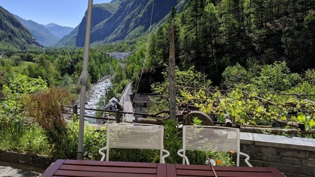 Une table et des chaises placées sous une tonnelle, offrant une vue sur un paysage montagneux et une rivière.