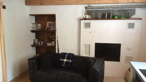 A cozy living room with a black leather sofa, wooden shelves with various items, a fireplace, and a wooden ceiling.