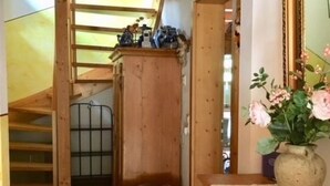 Interior de madeira com escada, cesta de vime e cômoda com um vaso de flores.