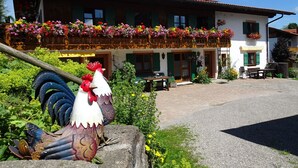 Een klassiek chalet met een balkon versierd met kleurrijke bloemen, een stenen beeldhouwwerk en een geplaveid binnenterrein.