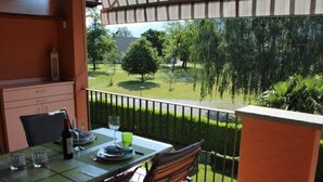 A balcony with a table set for two, chairs, and a view of a well-maintained garden. - Residenza al Mulin by Interhome (Ascona)