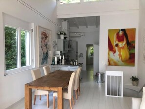 Ein großzügiger Essbereich mit Holztisch und weißen Stühlen, im Hintergrund eine Küche und ein großes abstraktes Gemälde an der Wand.