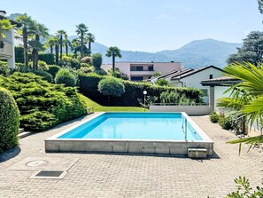 Ein rechteckiger Pool mit Pflasterdeck, umgeben von üppiger Vegetation und Blick auf Berge im Hintergrund.