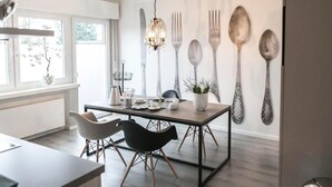 Een moderne keuken met een eettafel, twee stoelen, een kroonluchter en een wandmontage voor keukengerei.