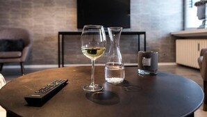 Een gezellige woonkamer met een ronde salontafel, een wijnglas, een waterglas, een afstandsbediening en een kaars.