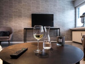 Ein gemütliches Wohnzimmer mit rundem Couchtisch, einem Weinglas, einem Wasserglas, einer Fernbedienung und einer Kerze.