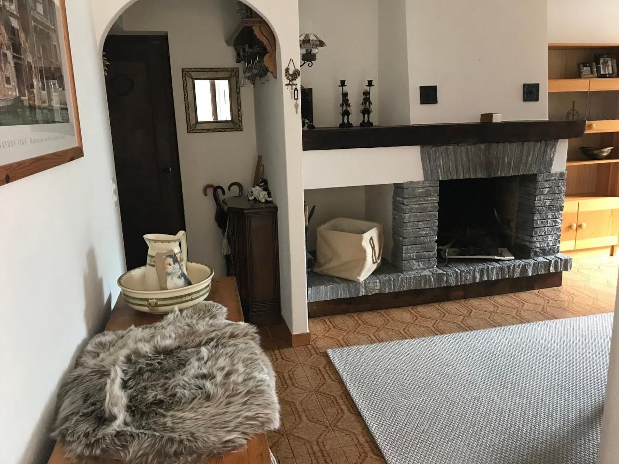 A cozy living room with a fireplace, a rug, a fur throw, and a bowl with a cat figurine.