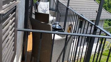 A balcony with wicker furniture, a metal railing, and a view of a house with a tiled roof and a chimney.