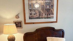 A bedroom with a bed, a nightstand, a lamp, and a framed picture of a canal scene.