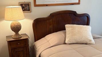 A bedroom with a bed, a nightstand, a lamp, and a framed picture of a canal scene.
