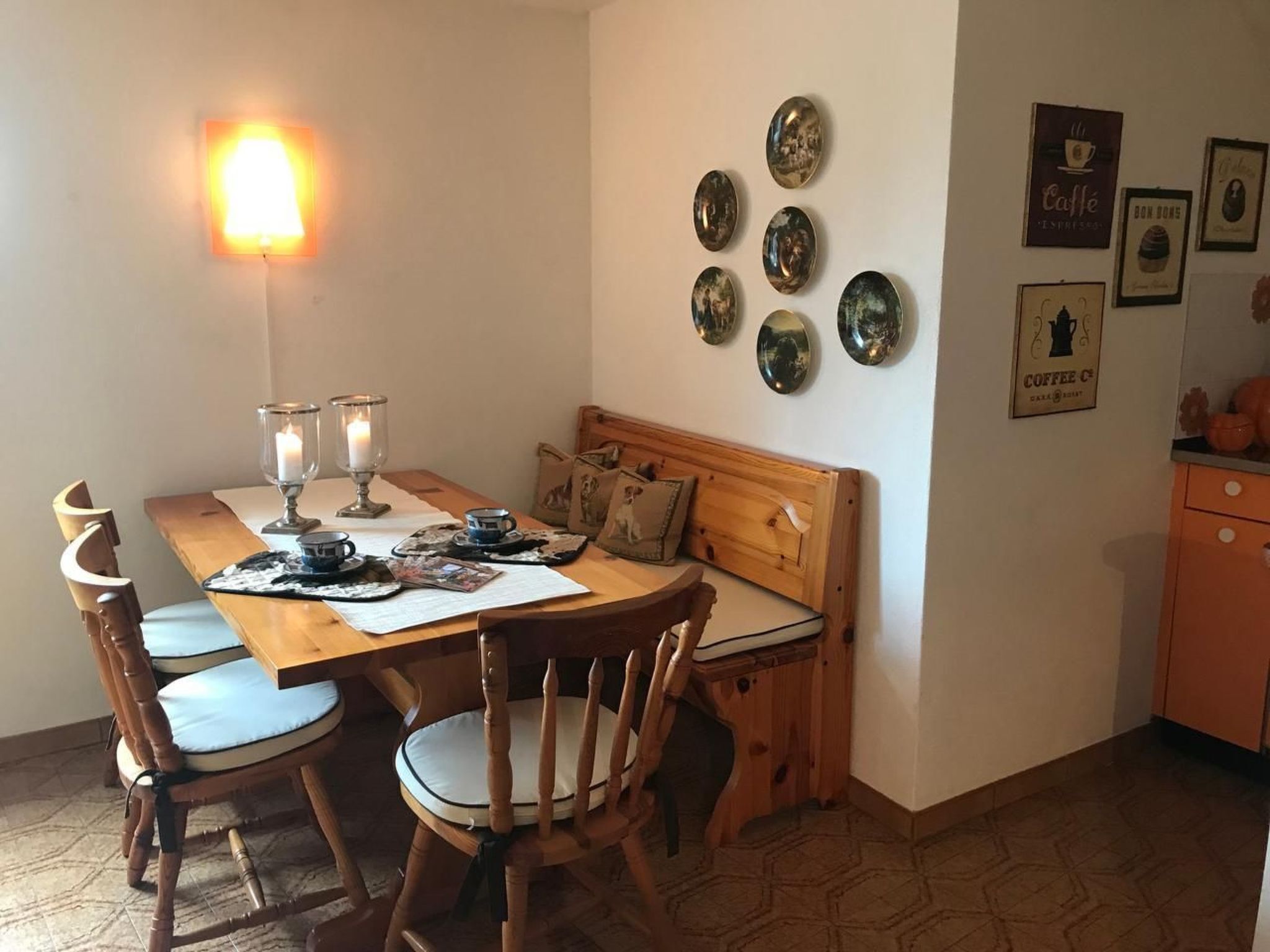 A cozy dining area with a wooden table, chairs, and a bench. There are wall-mounted plates and framed pictures on the wall.