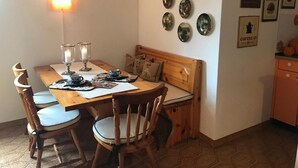 A cozy dining area with a wooden table, chairs, and a bench. There are wall-mounted plates and framed pictures on the wall.