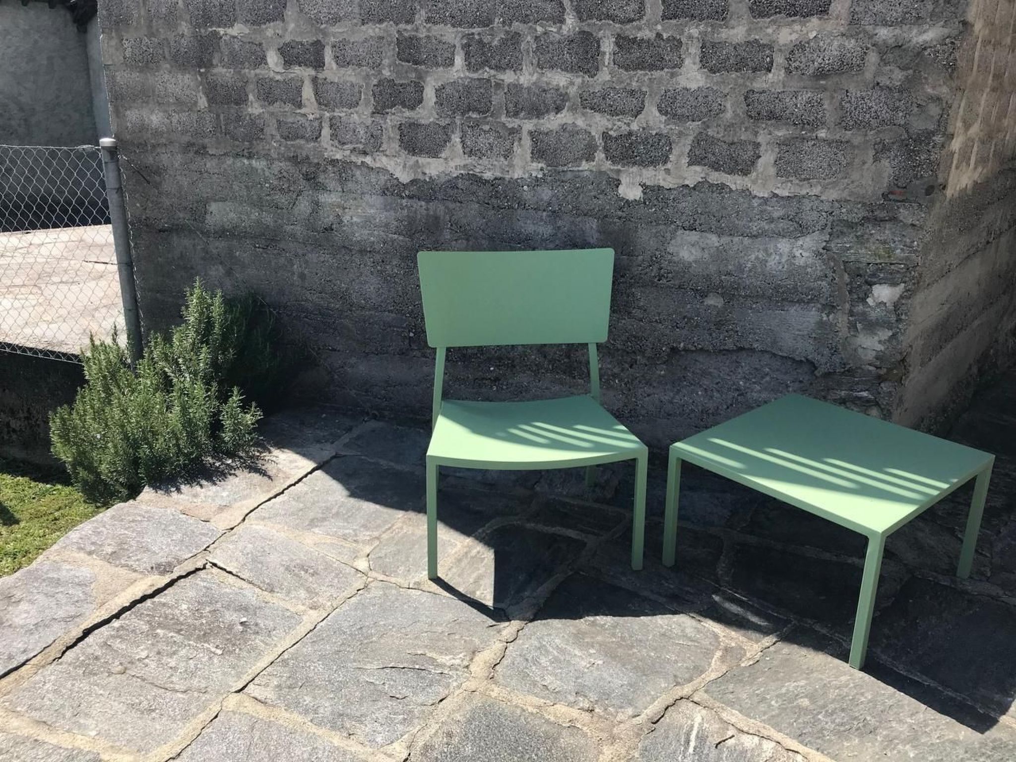 Um pátio de pedra com duas cadeiras verdes e uma pequena planta.