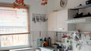 Ett kök med vita skåp, ett matbord med stolar, en spis och ett fönster med persienner.