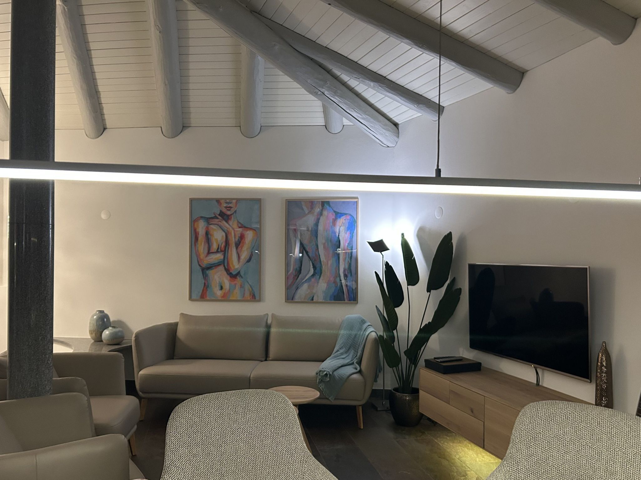 A modern living room with a sofa, armchairs, a TV, and abstract paintings.