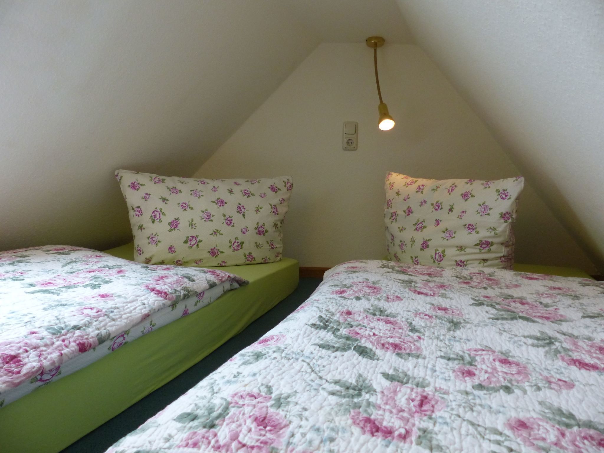 Una habitación pequeña y triangular con dos camas individuales, cada una con ropa de cama floral y almohadas a juego.