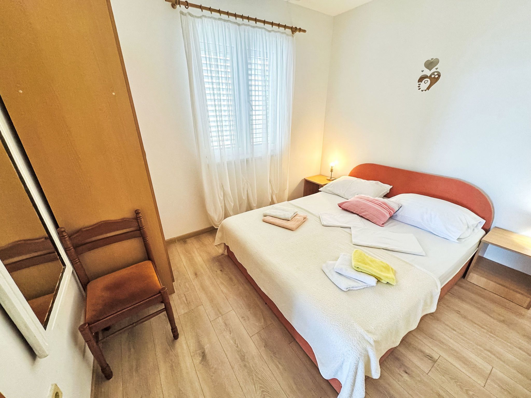 A bedroom with a bed, a chair, a window with curtains, and a wall-mounted light.