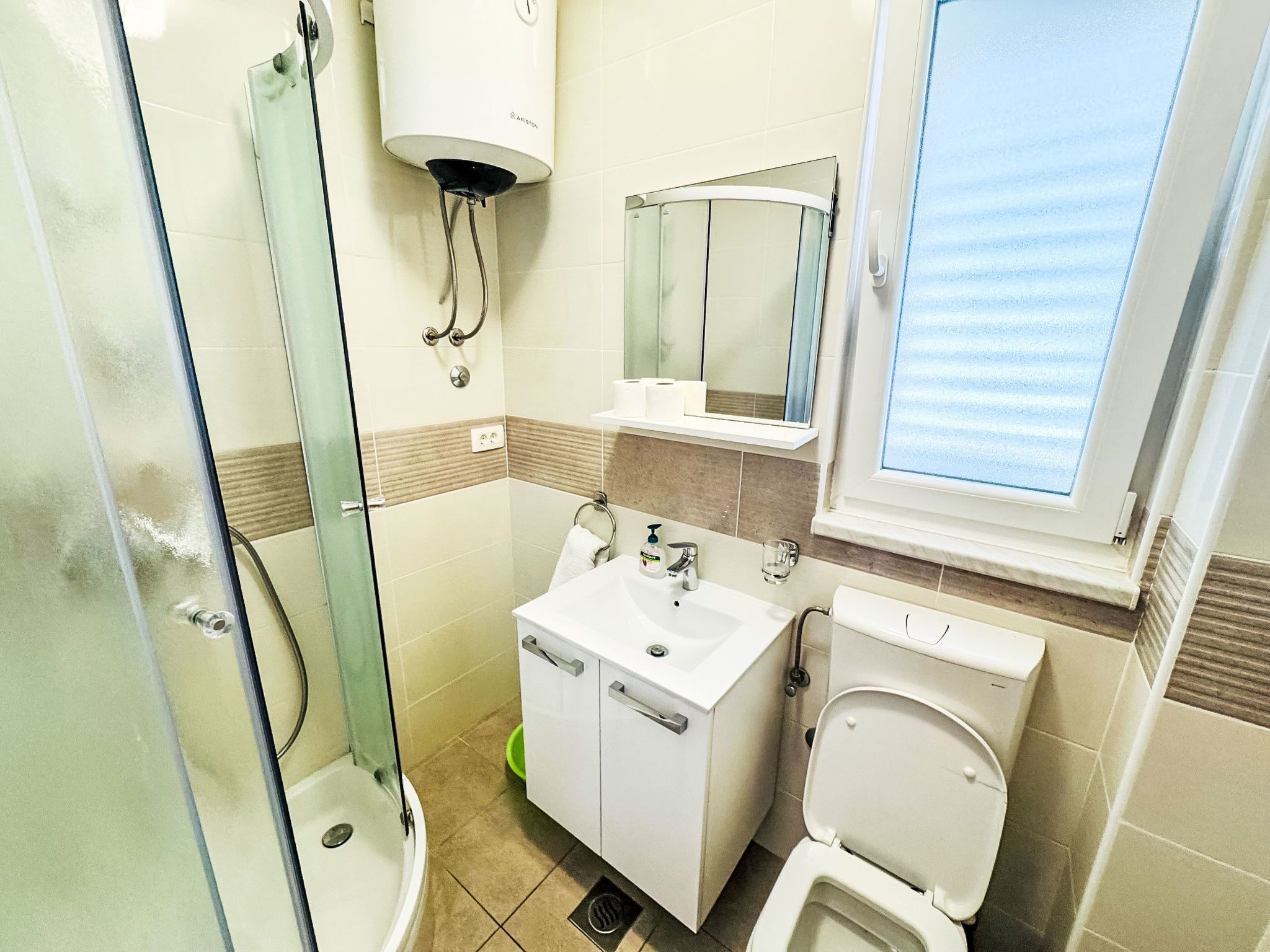 Un bagno con cabina doccia in vetro, lavabo bianco con specchio sopra e water.