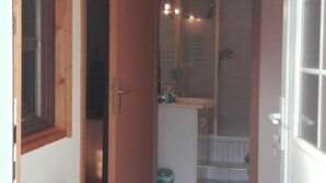 Un couloir étroit avec un plafond en bois, une porte sur la droite et une salle de bain avec une douche, un lavabo et des toilettes visibles à travers une porte en verre.