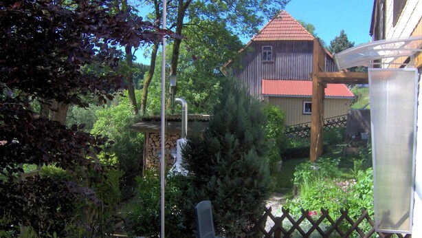 Une terrasse avec une table ronde et des chaises, entourée d’une clôture en bois et d’une végétation luxuriante.