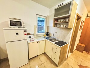 A compact kitchen with a refrigerator, microwave, sink, and a window with blinds. - Angenehme Wohnung in Komarna mit privatem Parkplatz by Interhome (Klek)
