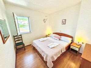 A bedroom with a bed, bedside tables, a chair, a window, and wall decorations. - Angenehme Wohnung in Komarna mit privatem Parkplatz by Interhome (Klek)