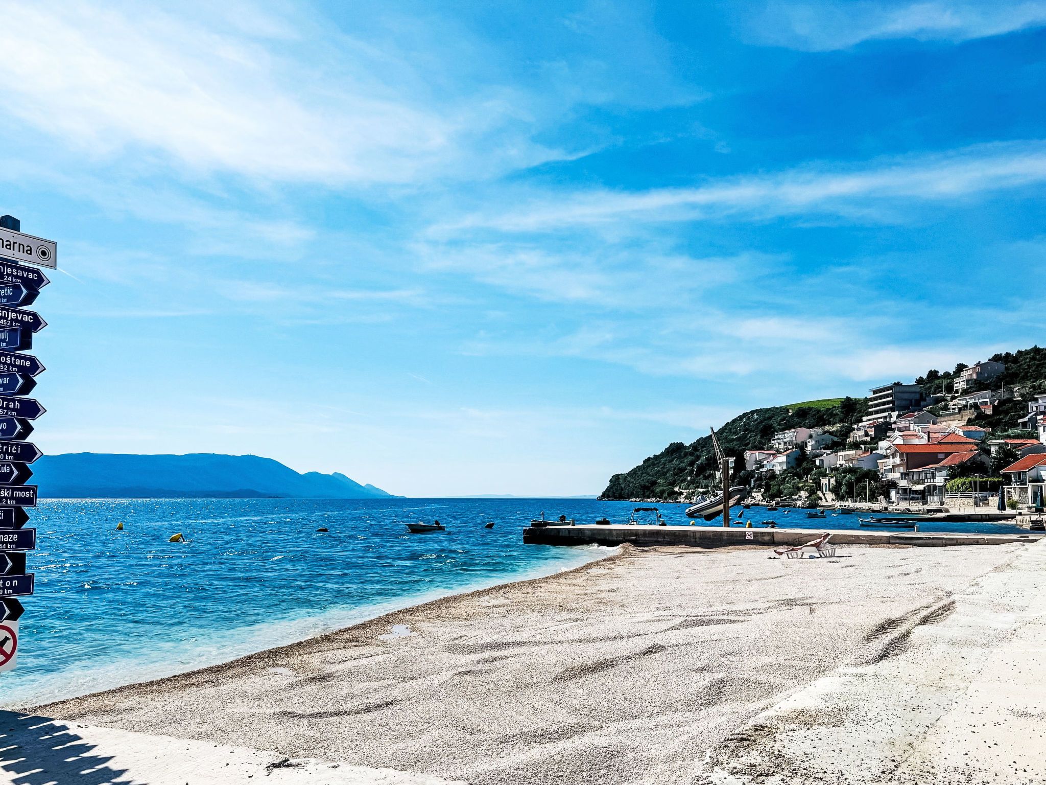 A coastal beach with a clear sky, a pebble beach, and a pier with boats.