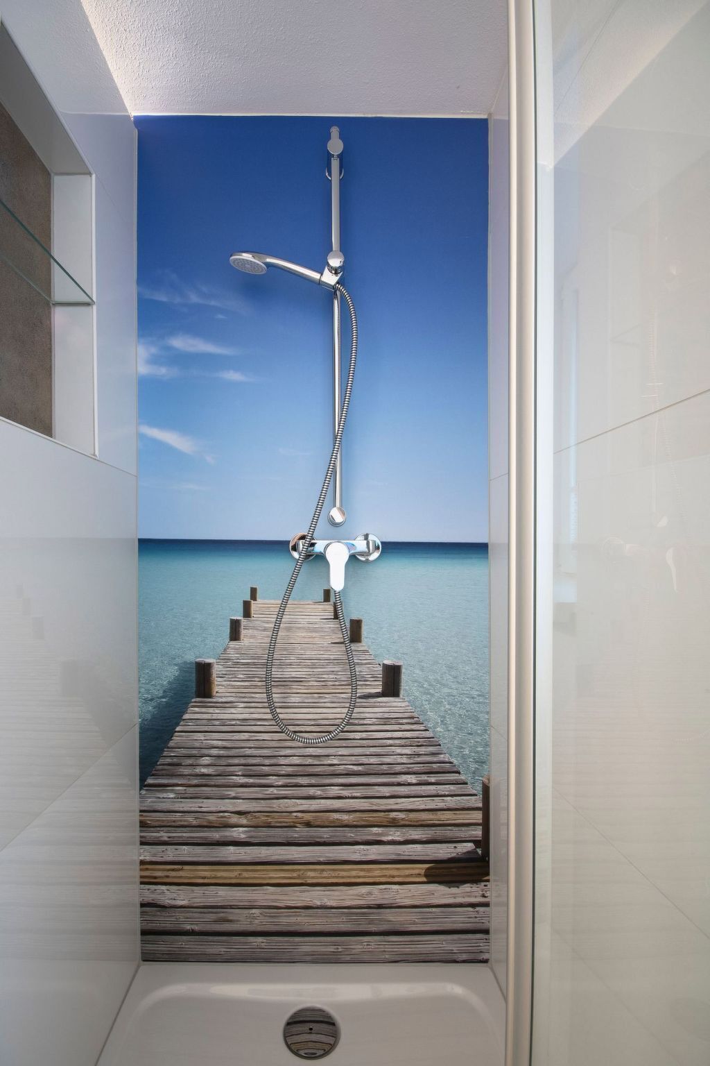 Une salle de bain moderne avec une douche et une vue sur une jetée en bois qui mène à une mer calme.