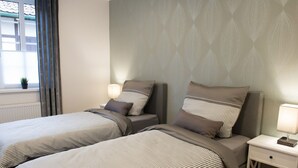A double bed with striped bedding, a bedside table with a lamp, and a window with curtains. - in Goslar mit Terrasse und Grill by Interhome (Goslar)