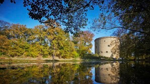 Et historisk stenhus ved en rolig sø, omgivet af efterårsblade.