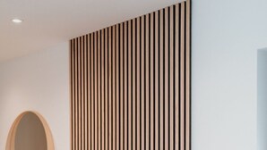 Una habitación moderna con pared de listones de madera, un espejo redondo, un radiador blanco y un banco de madera.