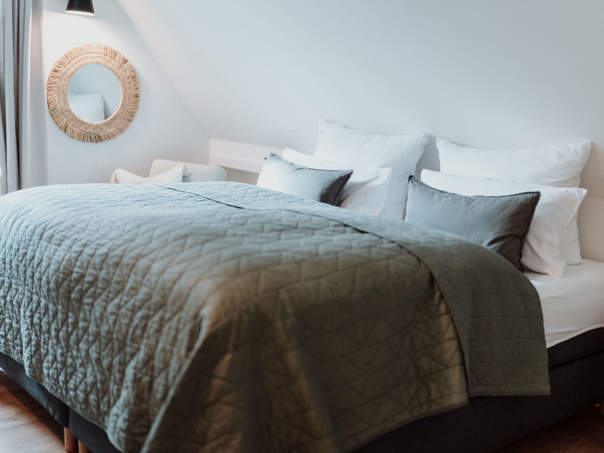 Ein ordentlich bezogenes Bett mit einer grünen Decke, weißen Kissen und einem runden Spiegel an der Wand.