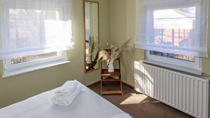 A bedroom with a bed, a radiator, a window with a sheer curtain, a mirror, and a small table with decorative plants. - in Alt-Schadow mit Grill und Terrasse by Interhome (Jessern)