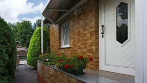 A house with a brick exterior, a white door, and a small window. There is a garden with flowers and a pathway leading to a gate. - in Alt-Schadow mit Grill und Terrasse by Interhome (Jessern)