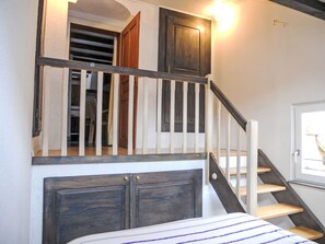 Escada que leva a um quarto no mezanino, com cama e janela.