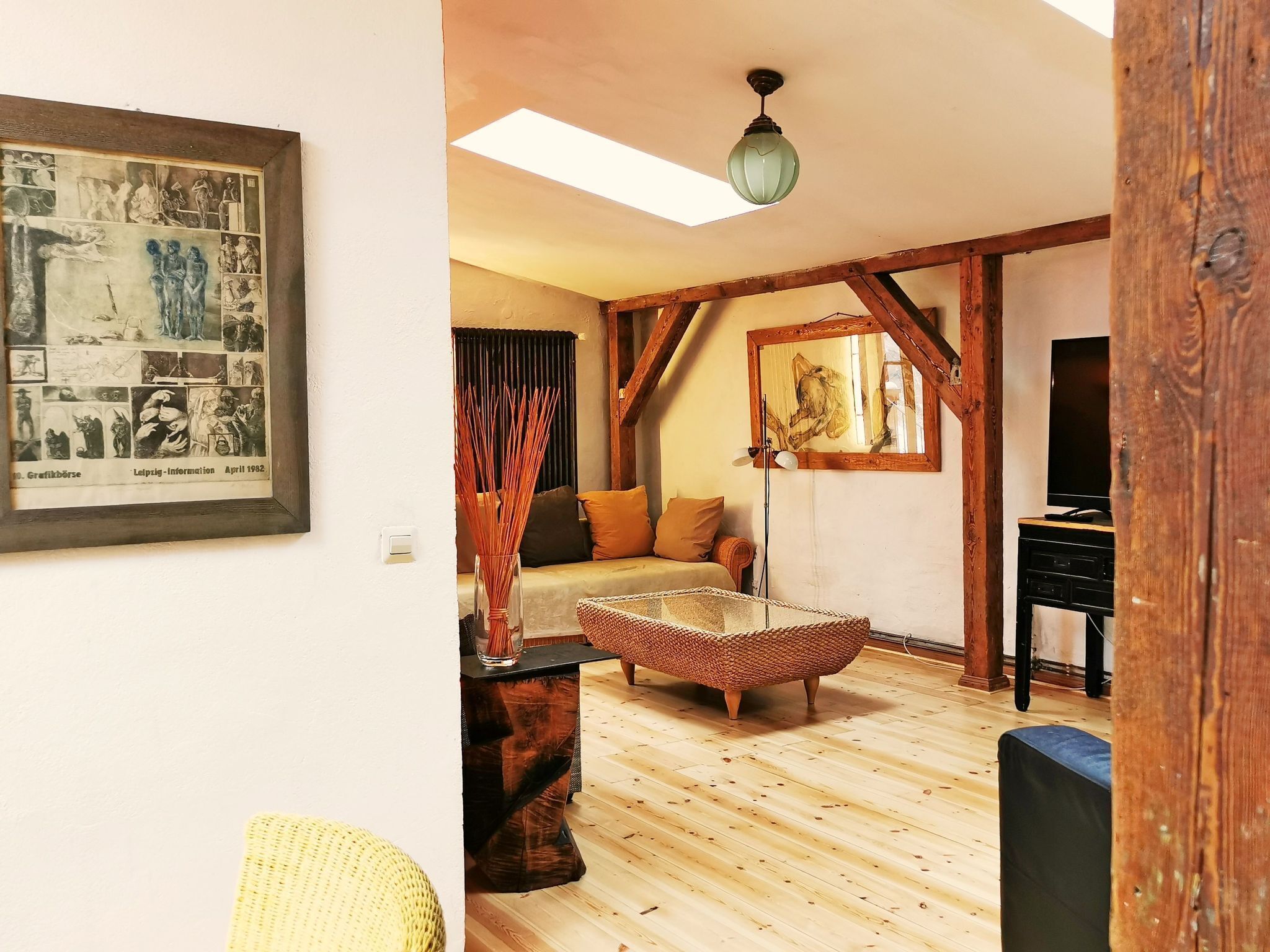 Ein gemütliches Zimmer mit Holzboden, einem gewebten Hocker, einer Couch und einem gerahmten Bild an der Wand.