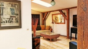 Een gezellige kamer met een houten vloer, een geweven poef, een bank en een ingelijst beeld aan de muur.